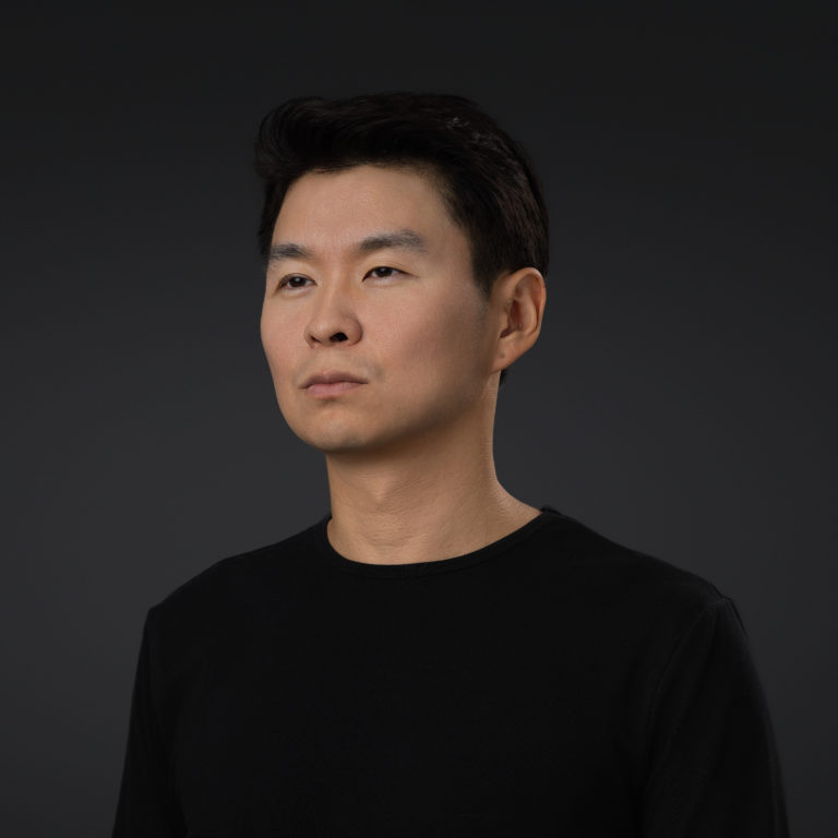 A professional headshot of a person not looking at the camera on a dark background using studio light.