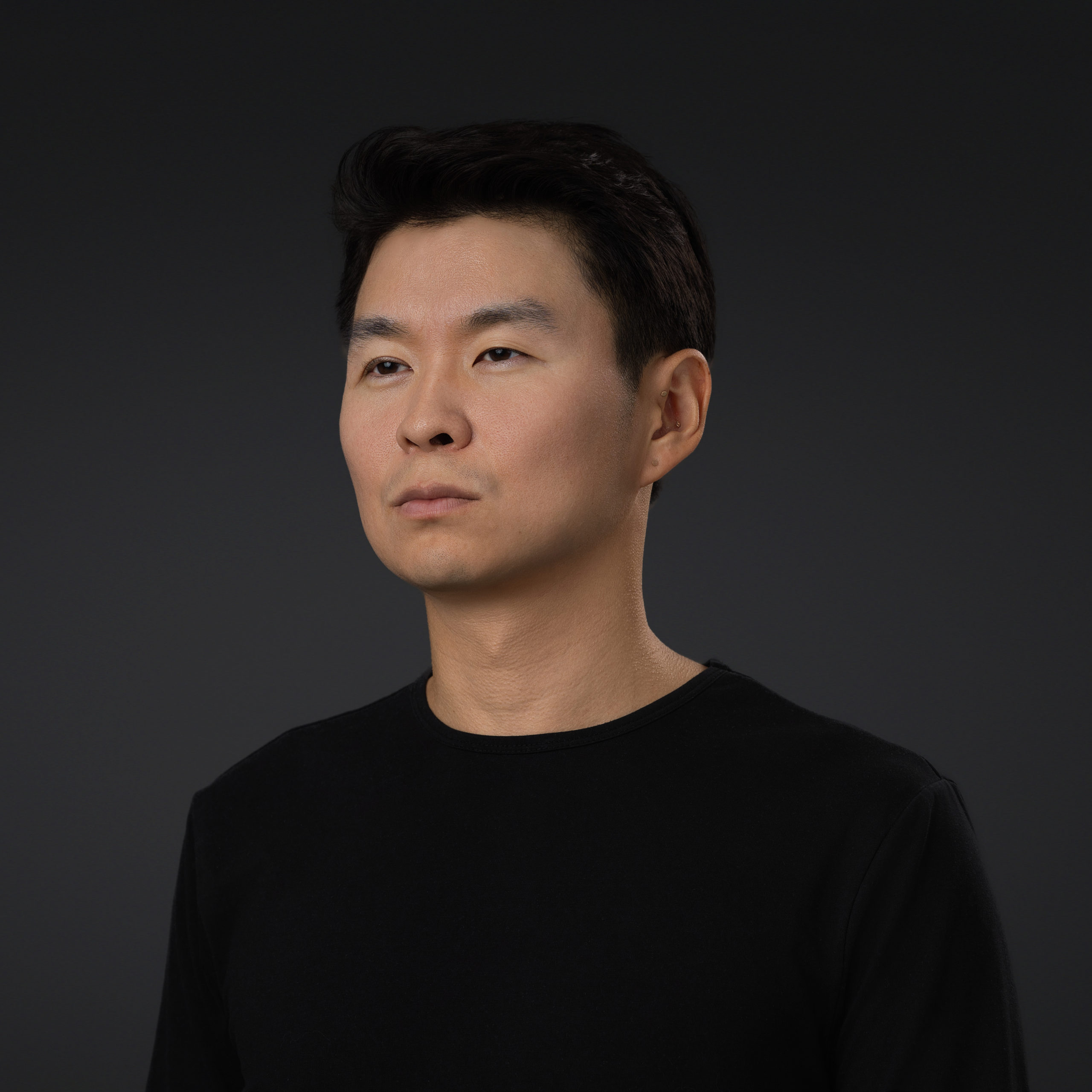 A professional headshot of a person not looking at the camera on a dark background using studio light.